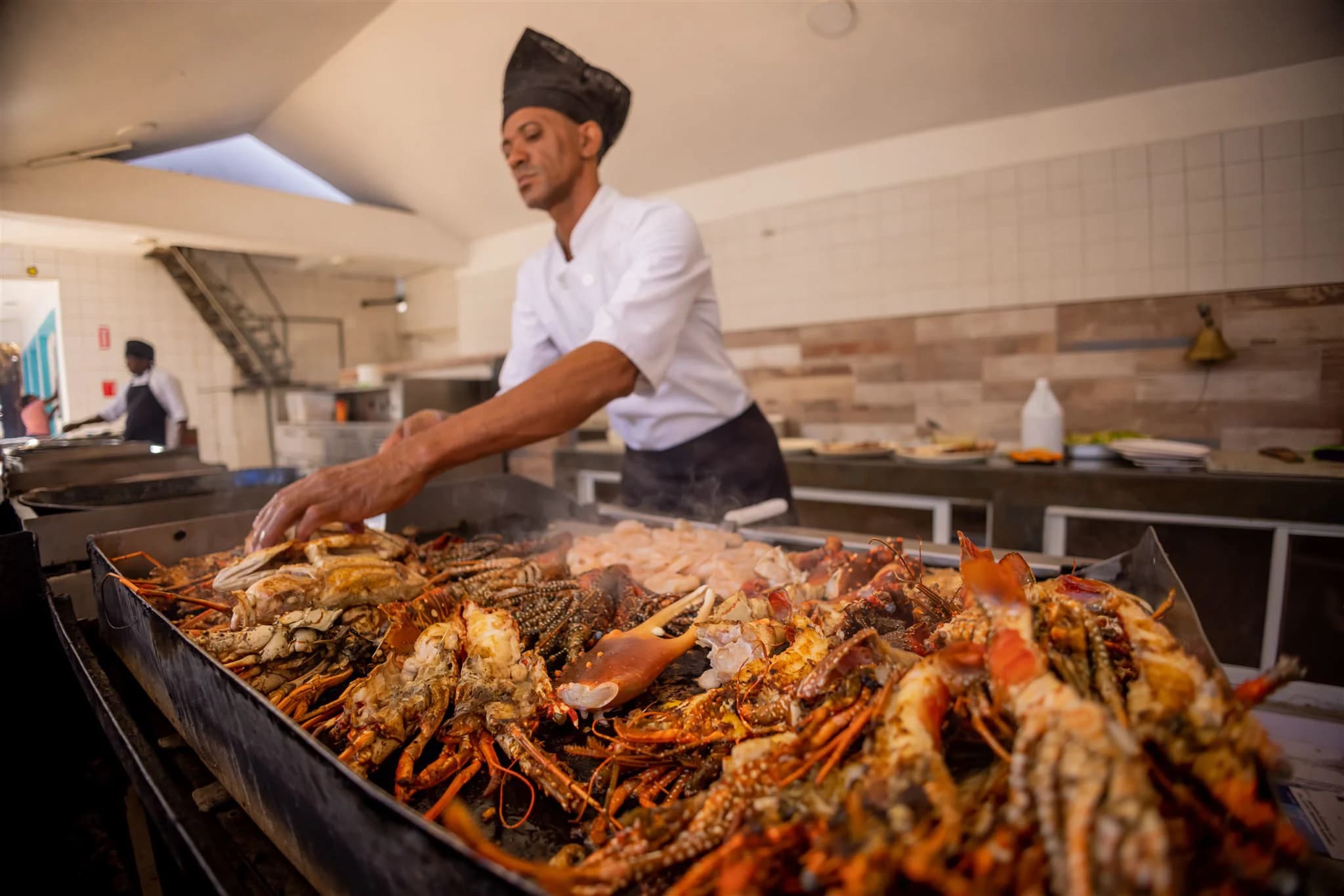Chef in a black hat tending a grill full of lobster and crab
