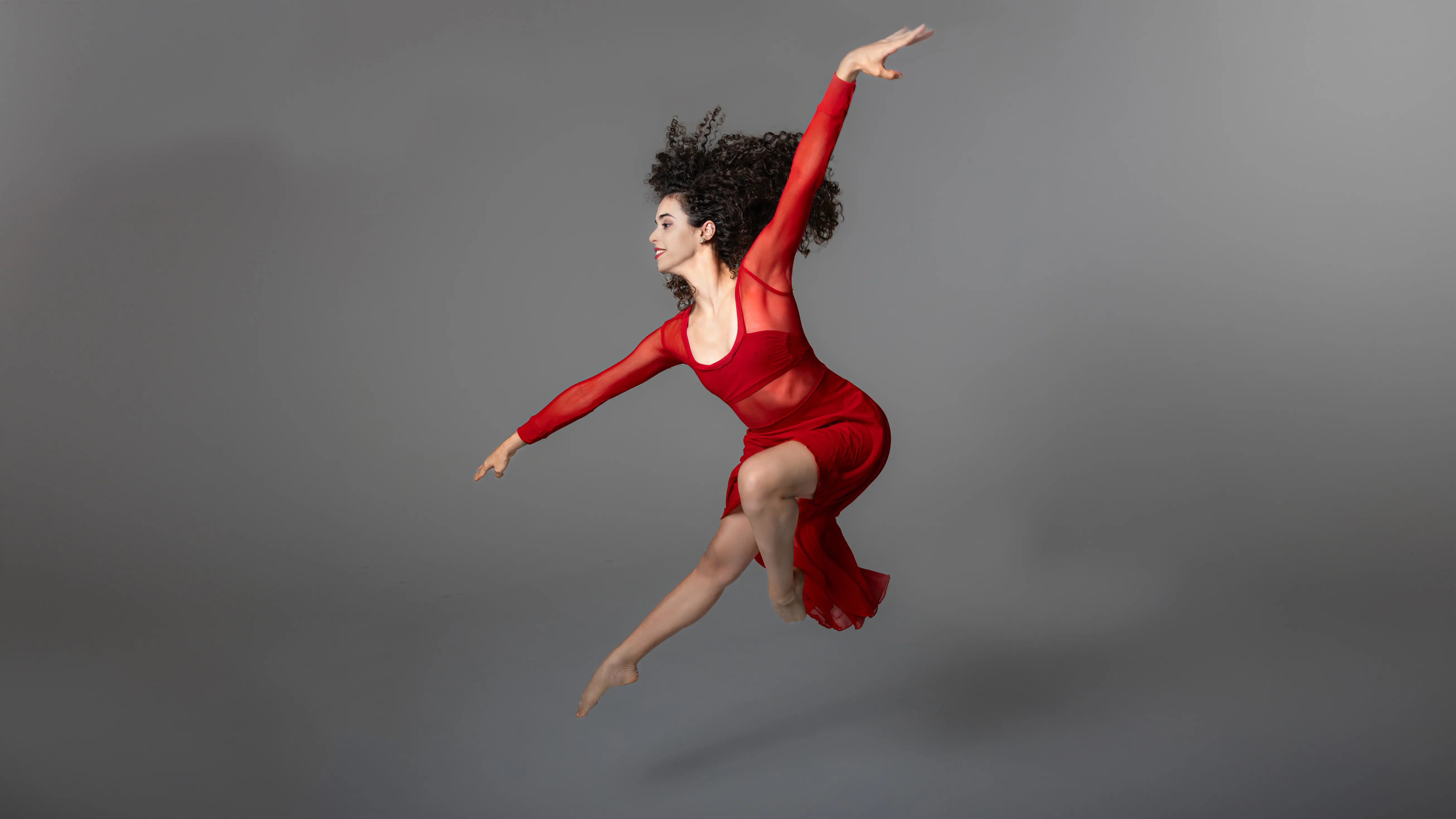 Dancer in flight — Artistic portrait Dancer in flight wearing red costume against neutral grey background; artistic movement photography in Santo Domingo studio