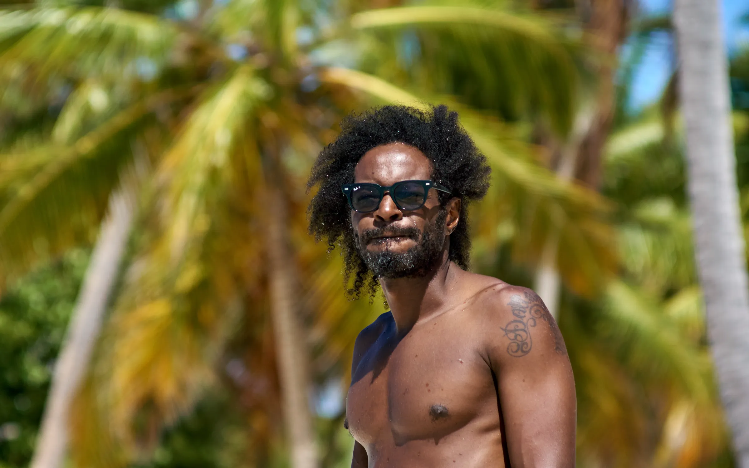 Luxury Portrait on Tropical Beach Man wearing dark sunglasses posing on tropical beach with blurred palm foliage, luxury portrait session in Punta Cana, Dominican Republic